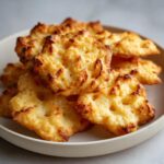 A close-up pile of golden brown, crispy, homemade cheese crackers stacked on a light-colored plate.