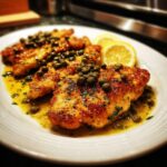 Close-up of golden brown chicken piccata fillets swimming in lemon-butter sauce and topped generously with capers.