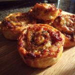 Close-up of several golden brown, baked pizza pinwheels sprinkled with herbs on a wooden cutting board.