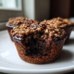 Close-up of a gooey pecan pie muffins with a bite removed, showing the dark interior and pecan crumble topping.