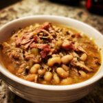 Close-up of a white bowl filled with a savory black eyed peas recipe topped generously with shredded ham and broth.