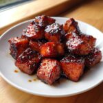 Close-up of glistening, caramelized honey garlic salmon bites piled on a white plate.