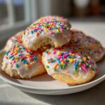 A stack of soft Italian ricotta cookies topped with white glaze and colorful sprinkles, one has a bite taken out.