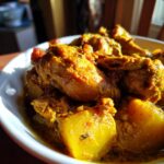 A close-up, appetizing shot of Jamaican curry chicken pieces and large potato chunks simmering in a rich, yellow curry sauce.