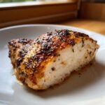 Cross-section of a perfectly cooked piece of greek chicken showing moist white meat and a flavorful, browned herb crust.