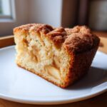 A close-up of a moist slice of apple cake featuring visible apple chunks and a sugary cinnamon crust.