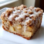 Close-up of a moist slice of apple crumb cake topped with brown sugar streusel and vanilla glaze.