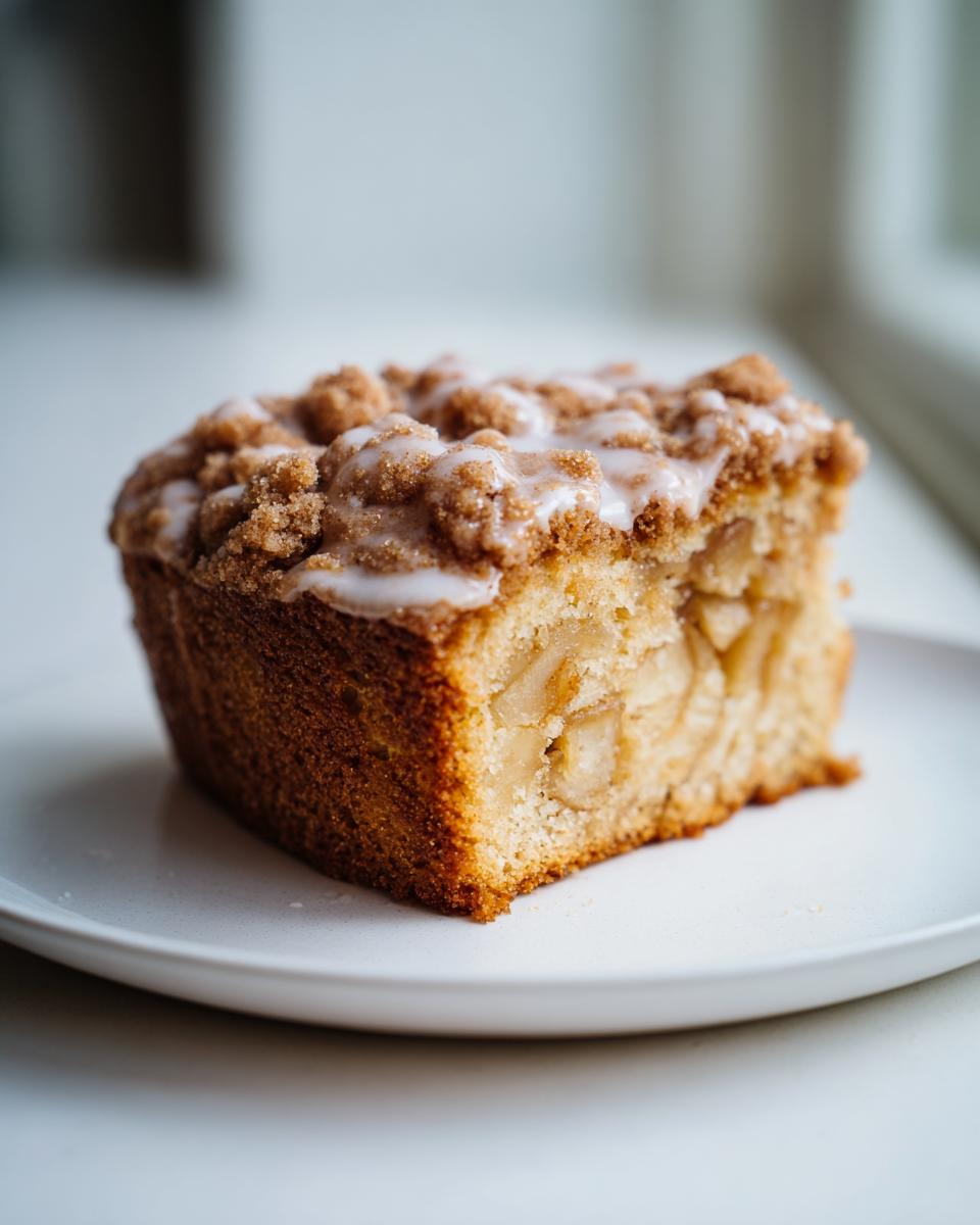A close-up of a single, moist slice of apple crumb cake topped with brown sugar crumble and vanilla glaze.