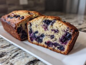 Close-up of moist blueberry banana bread sliced open, showing rich purple blueberries throughout the crumb.
