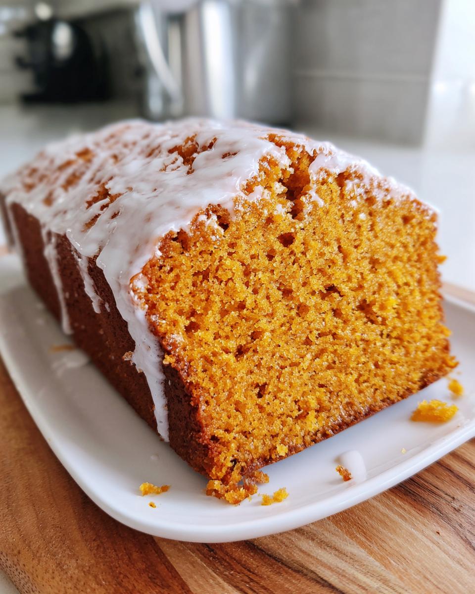 Close-up of a moist sweet potato pound cake loaf, sliced to show the orange crumb and topped with a white vanilla glaze.