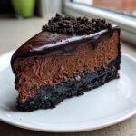 A rich slice of no bake chocolate cheesecake featuring a dark cookie crust, thick mousse layer, and chocolate ganache topping.