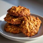 A close-up stack of golden brown, textured oatmeal breakfast cookie on a white plate.