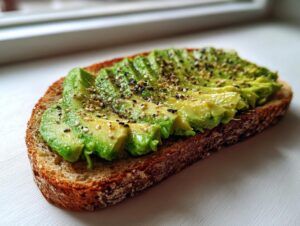 Close-up of perfectly sliced avocado toast on dark bread, topped generously with everything bagel seasoning.