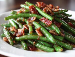 A close-up of bright green beans tossed in a savory glaze and topped with crispy bacon pieces.