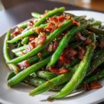 Close-up of vibrant green beans tossed with crispy bacon bits and a savory glaze.