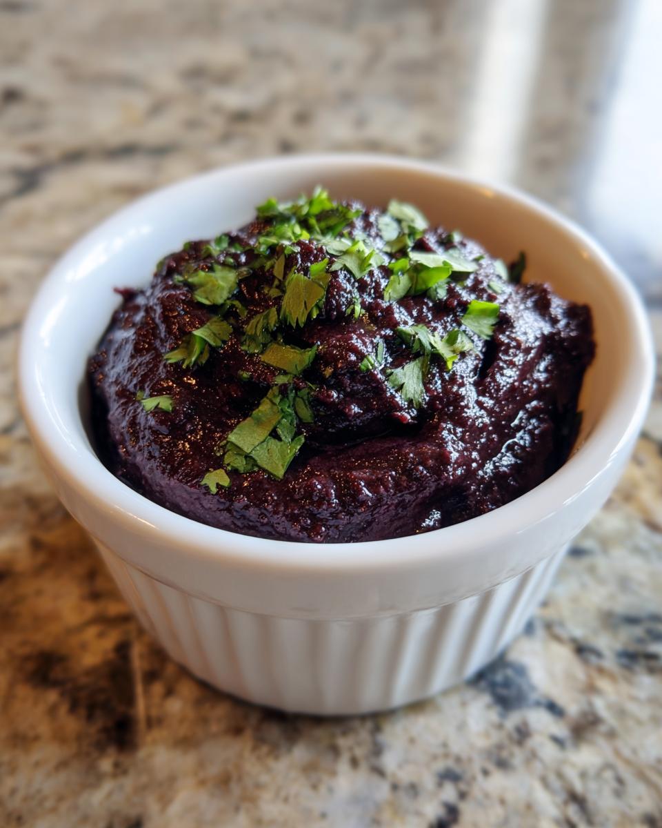 A close-up of rich, dark purple black bean dip topped with fresh cilantro in a white ramekin.