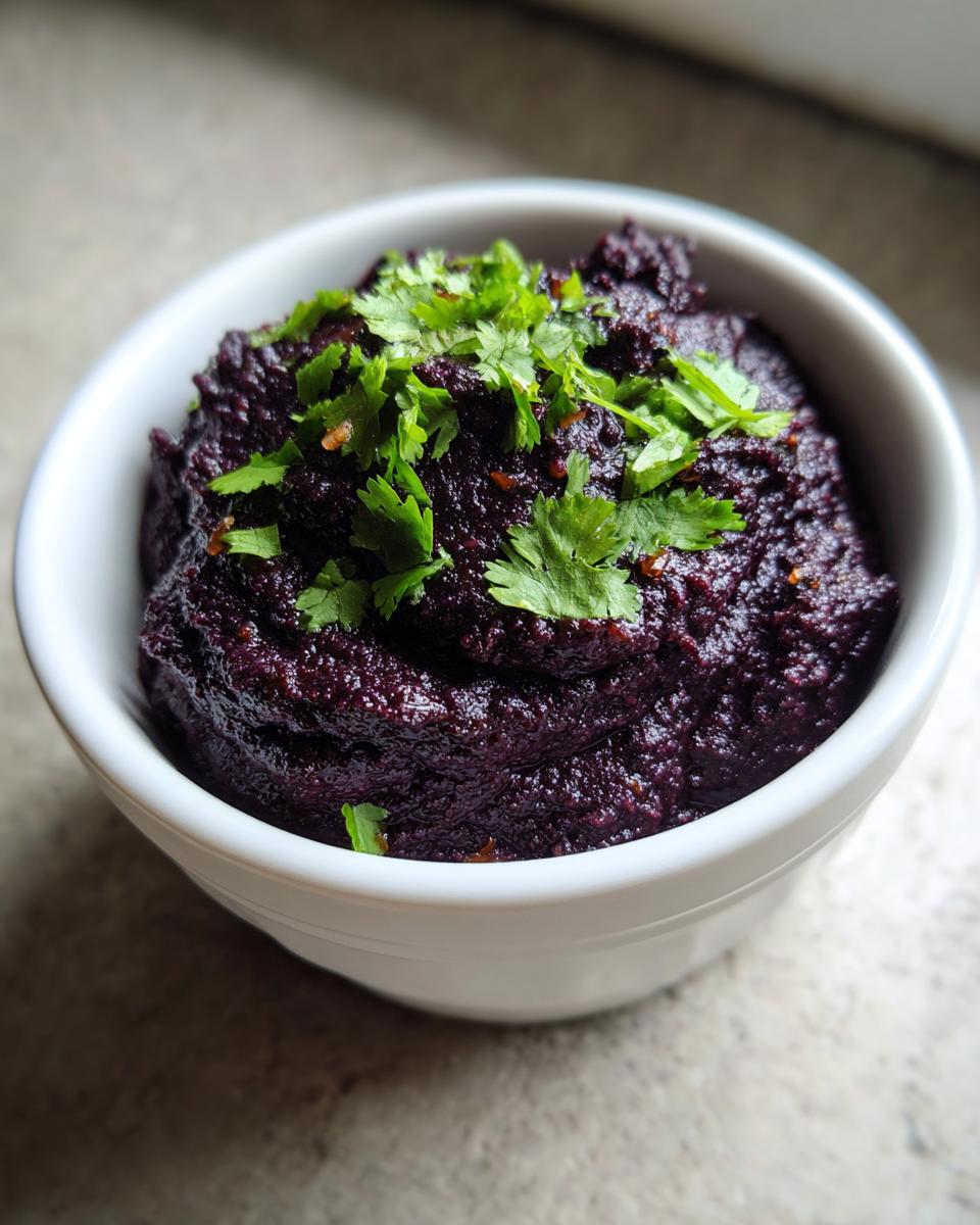 Close-up of a rich, dark purple black bean dip topped with fresh cilantro in a small white bowl.
