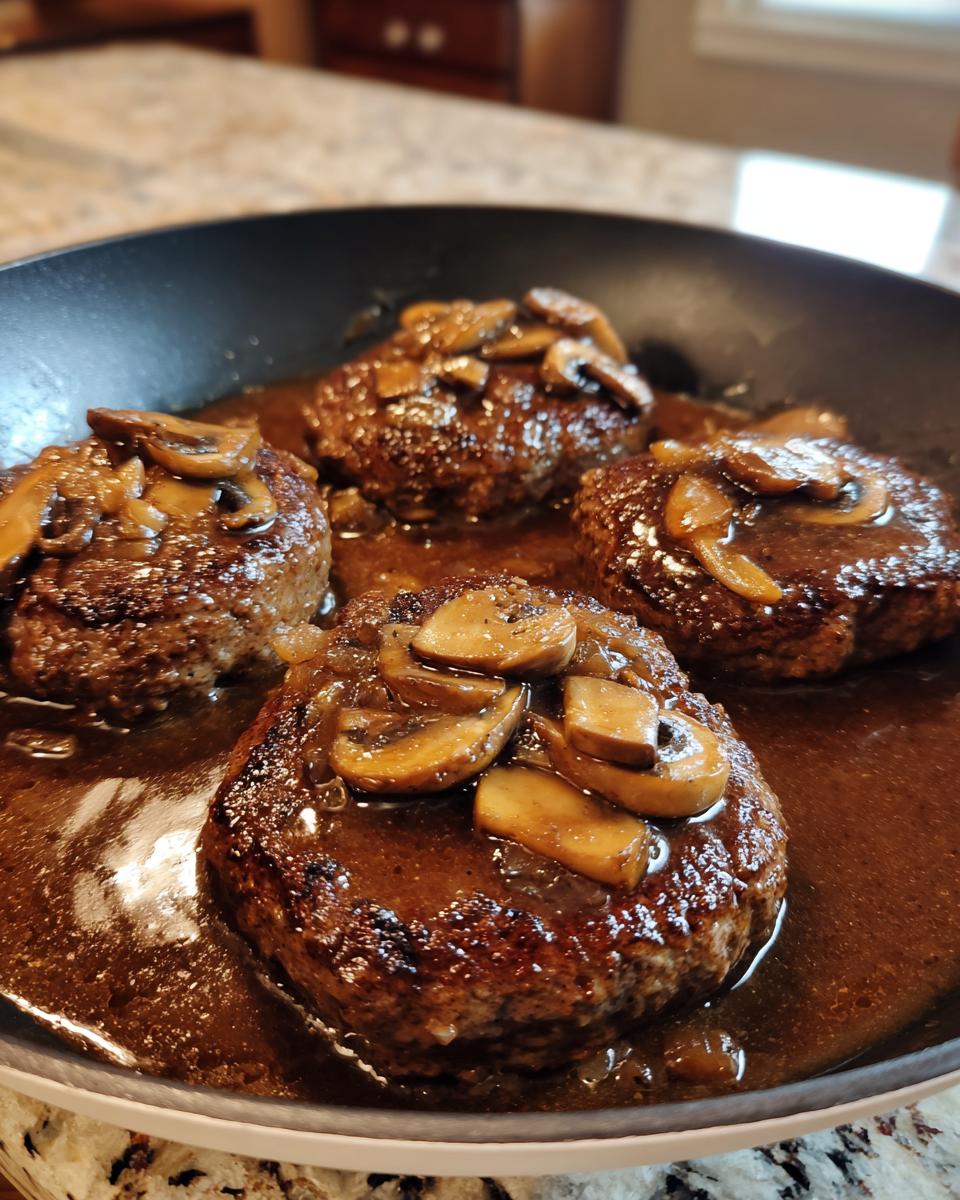 Four perfectly seared salisbury steak patties covered in rich brown mushroom gravy.