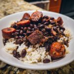 A close-up of a white bowl filled with savory black beans and rice topped with slices of browned sausage.