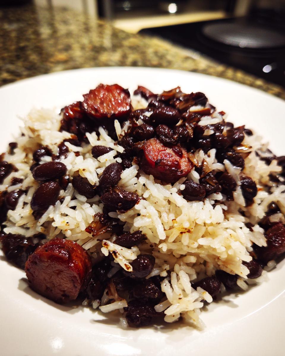 A close-up of a serving of black beans and rice mixed with sliced, browned sausage on a white plate.