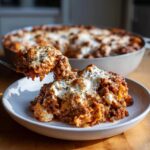 A spoonful of cheesy, meaty skillet lasagna being lifted above a serving on a plate.