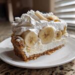 A generous slice of banana cream cheesecake featuring a graham cracker crust, creamy filling, fresh banana slices, and whipped cream topping.