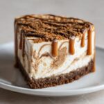A decadent slice of biscoff cheesecake with caramel drizzle and cookie crumbs on top.