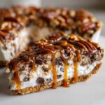 A decadent slice of texas trash pie featuring a creamy filling, chocolate chips, nuts, and a thick caramel drizzle.