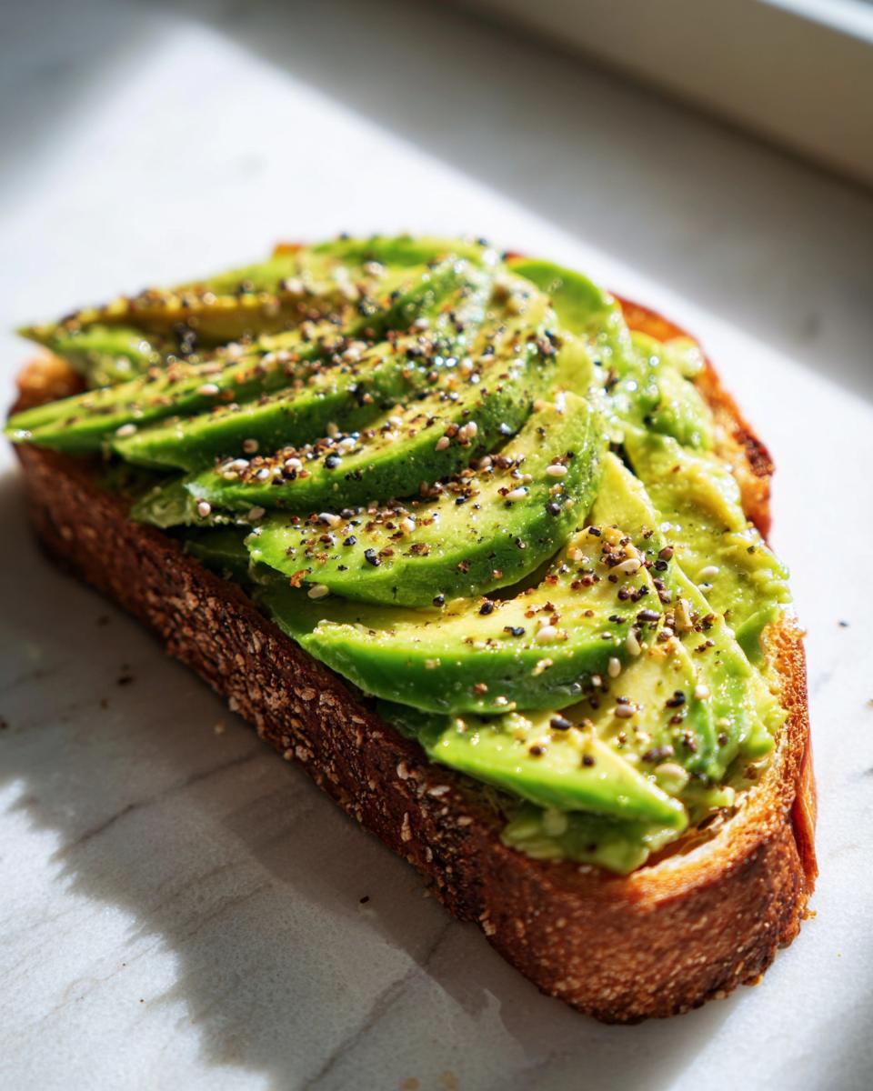 Close-up of perfectly sliced avocado toast on dark, toasted bread, sprinkled heavily with everything bagel seasoning.