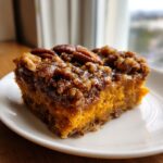 A close-up of a square slice of rich, orange southern sweet potato casserole topped with a crunchy pecan streusel.