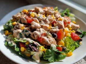 Close-up of a fresh southwest chicken salad featuring seasoned chicken, corn, black beans, tomatoes, and creamy dressing over lettuce.