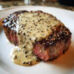 Close-up of a medium-rare steak generously covered in creamy peppercorn sauce.