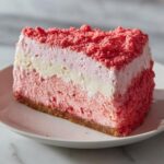 A perfect slice of strawberry crunch cheesecake showing layers of pink and white filling and a graham cracker crust.