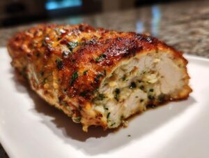 A close-up of a cooked, stuffed caesar chicken breast cut in half, showing the moist interior and browned, herbed exterior.