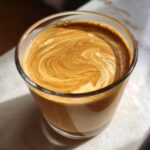 Close-up of a creamy, swirled top on a peanut butter banana smoothie in a glass.