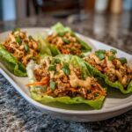 Four servings of thai chicken lettuce wraps filled with ground chicken, shredded carrots, and drizzled with a creamy sauce.