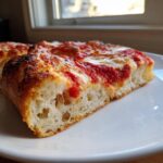 Close-up of a thick, airy slice of homemade pizza showing the fluffy crust, bright red sauce, and melted cheese.