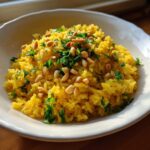 A bowl of vibrant yellow mediterranean rice topped with toasted pine nuts and fresh chopped parsley.