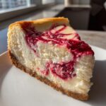 A perfect slice of white chocolate raspberry cheesecake with a graham cracker crust, featuring a vibrant raspberry swirl.