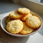 A close-up of several golden, textured 3-ingredient butter cookies piled in a light-colored bowl.