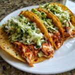 Three crispy shell salmon tacos filled with seasoned, flaked salmon and topped with fresh cabbage slaw and avocado.