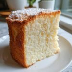 Close-up of a perfectly baked slice of angel food cake showing its airy texture, topped with powdered sugar.
