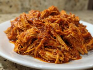A mound of saucy, shredded pulled chicken piled high on a white plate.