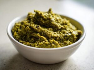 A close-up, featured image of thick, vibrant green olive dip mounded high in a small white bowl.
