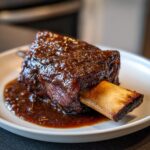 Close-up of a single, tender braised short ribs piece covered in a rich, dark glaze, resting in sauce.
