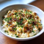 Creamy caramelized onion dip topped with rich caramelized onions and fresh green chives in a white bowl.