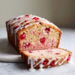 A slice cut from a loaf of moist cherry cake topped with a white vanilla glaze.