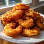 A close-up of a generous pile of perfectly golden brown fried shrimp stacked on a white plate.