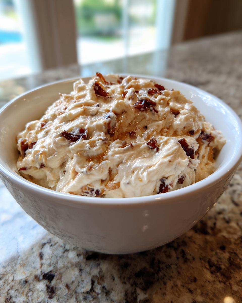 A close-up of creamy onion dip topped with crispy bacon pieces served in a white bowl.