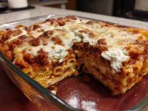 Close-up of a baked pasta bake in a glass dish, showing layers of ziti pasta, rich meat sauce, and melted cheese topping.